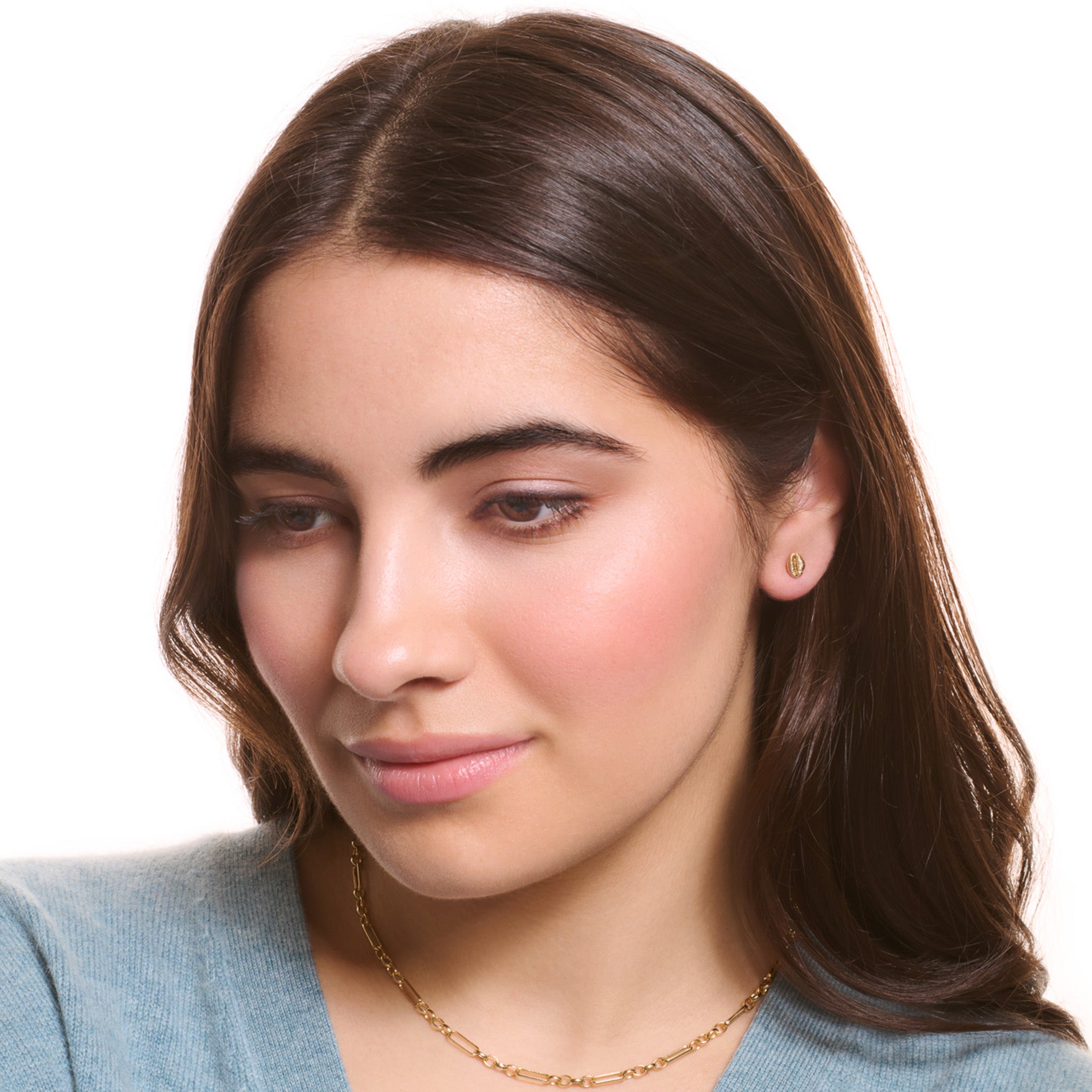 Model wearing handcrafted yellow gold earring studs showcasing a cowrie shell.