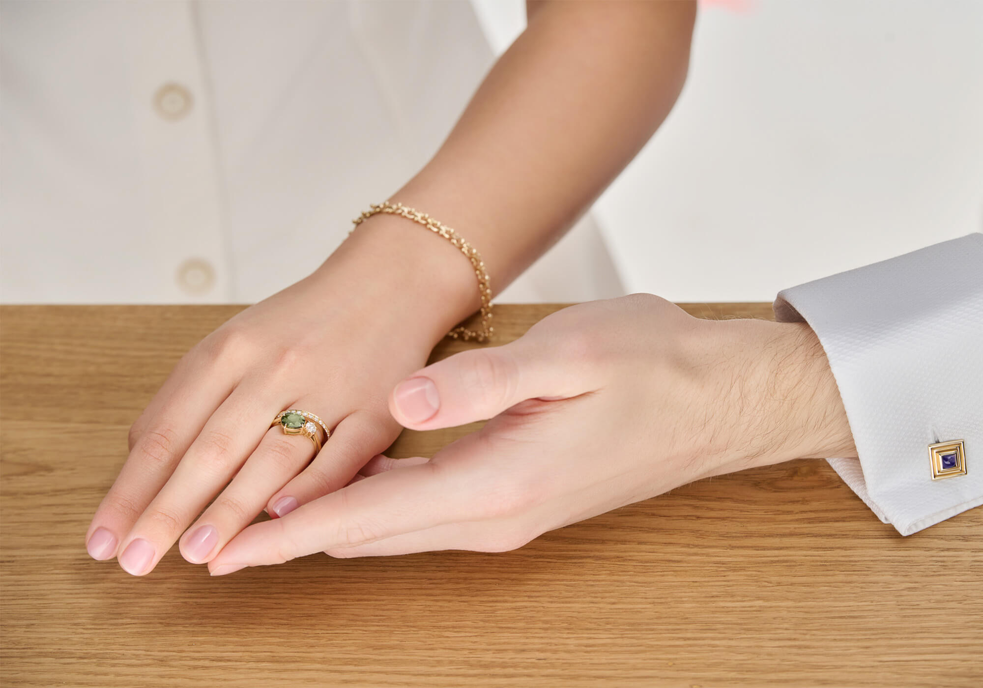 A woman's hand resting in a man's hand, showcasing an 18ct yellow gold engagement ring adorned with precious stones.