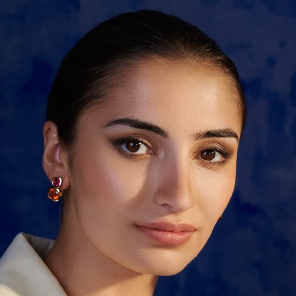 Model wearing handcrafted 18ct yellow gold square shaped earrings featuring pink tourmaline and fire opal gemstones.
