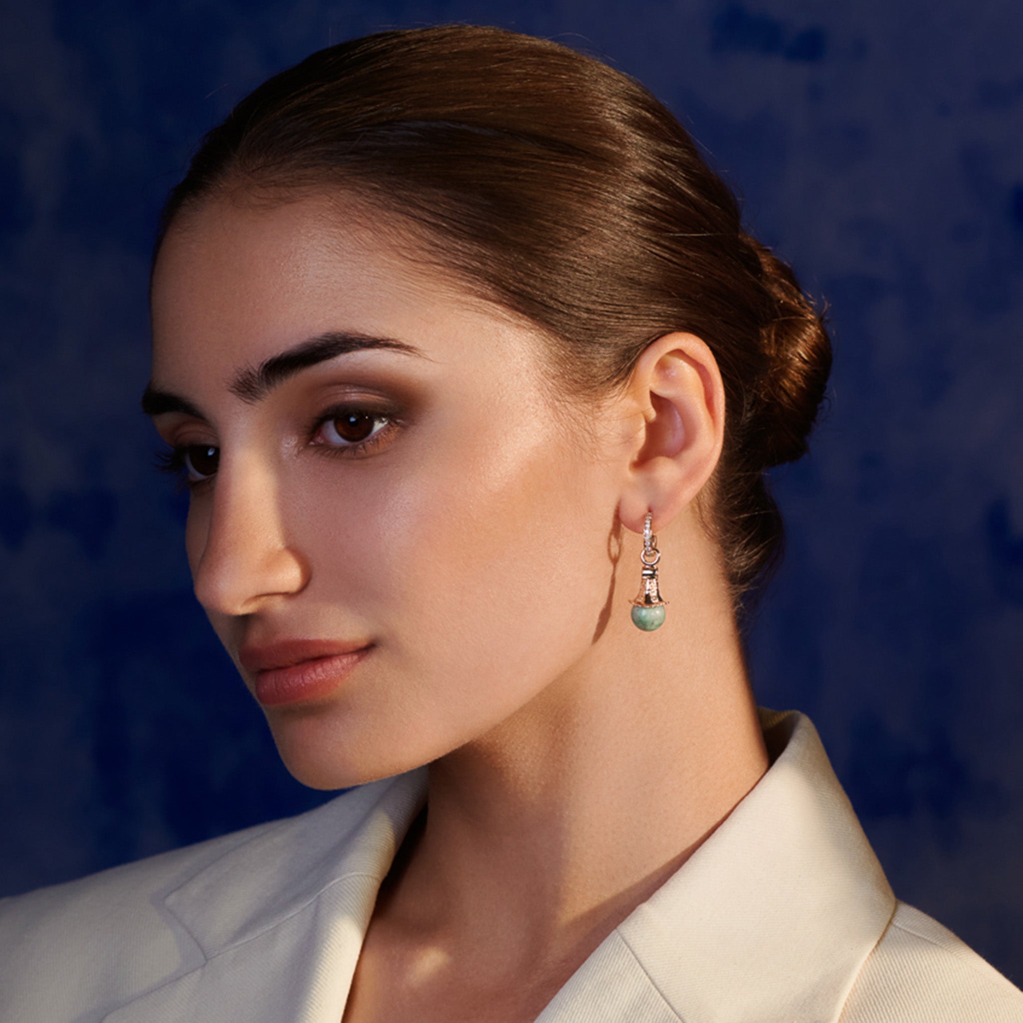 Model wearing handcrafted earring drops in precious metal with a precious stone.