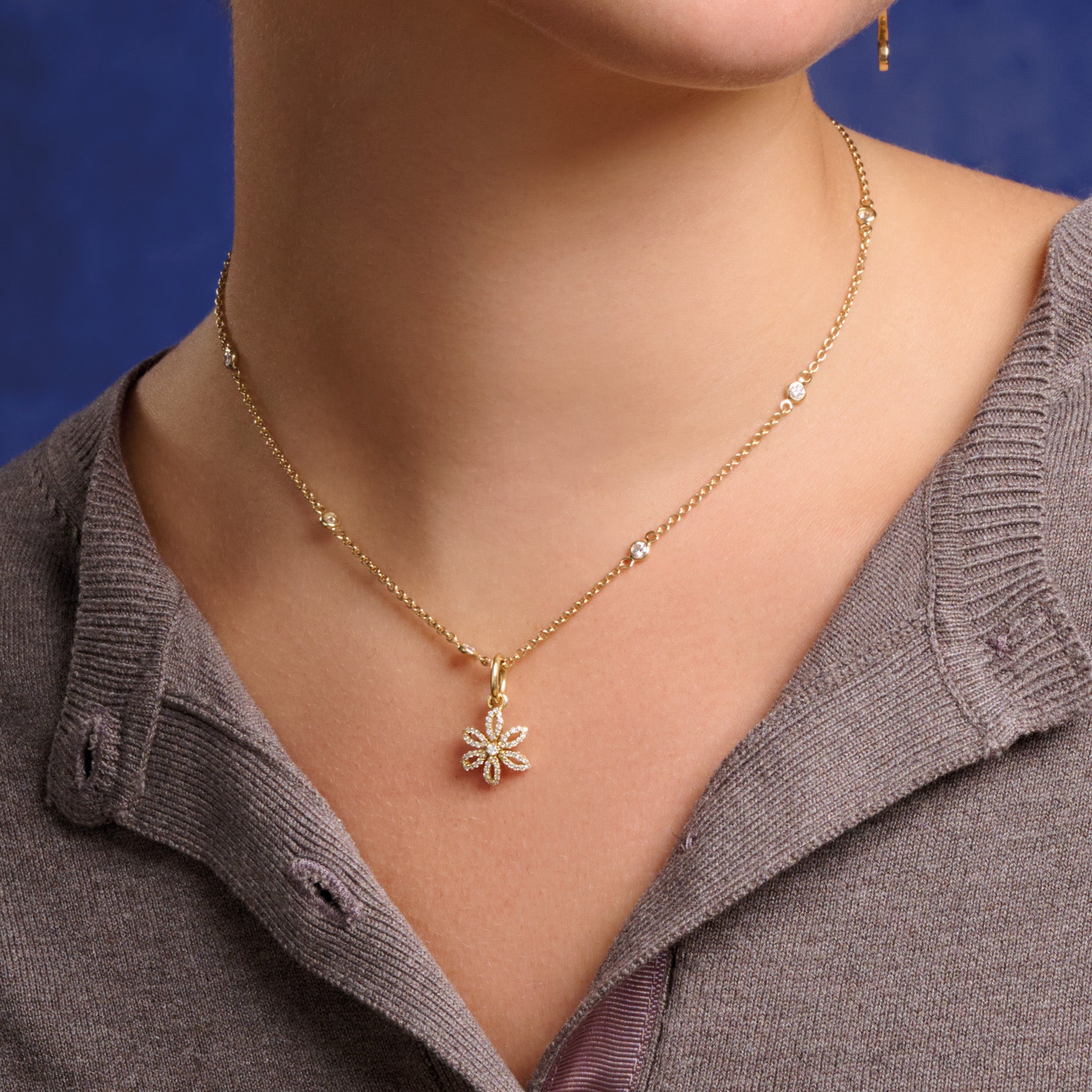 Model wearing handcrafted 18ct yellow gold flower necklace pendant with diamond pavé and central diamond, birthstone of April.