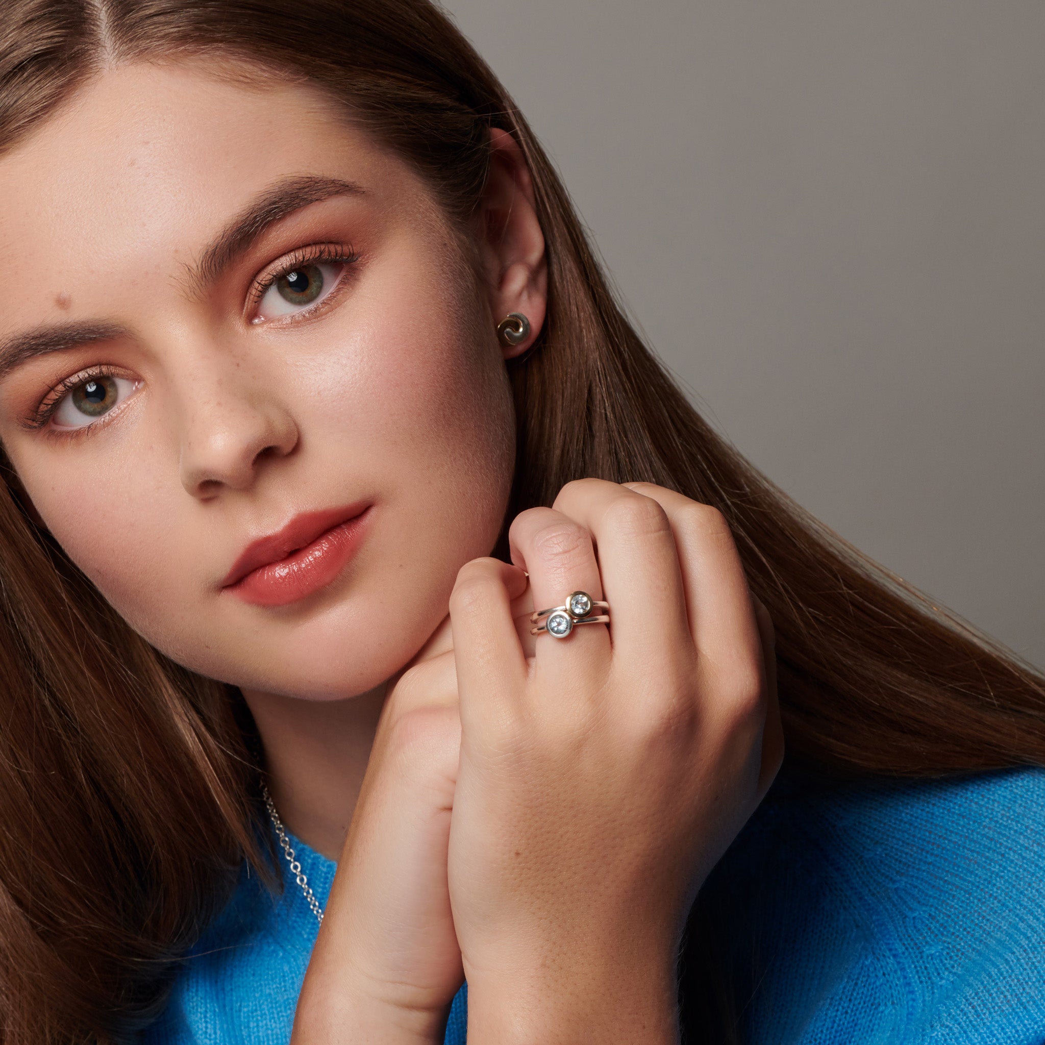 Model wearing two handcrafted rings in precious metal with central precious stones.