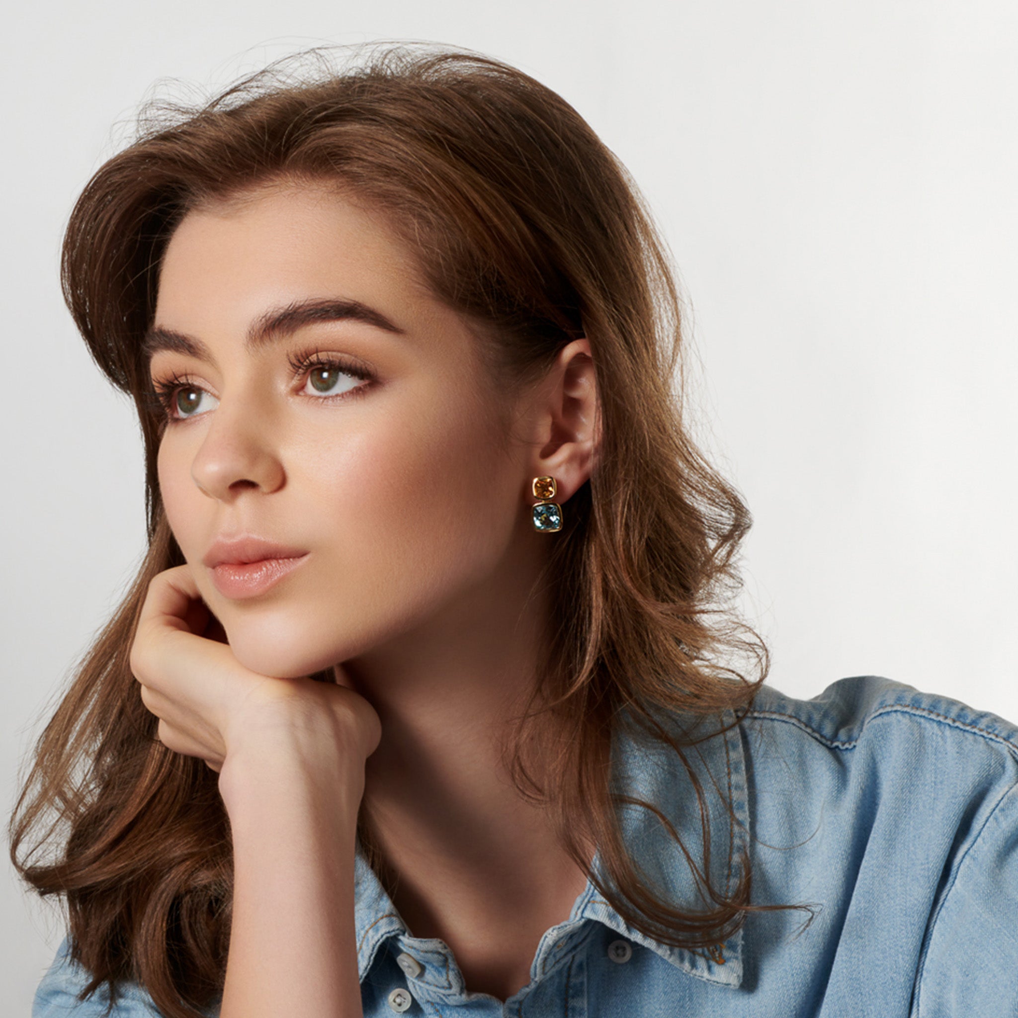 Model wearing handcrafted 18ct yellow gold square shaped earrings featuring precious gemstones.
