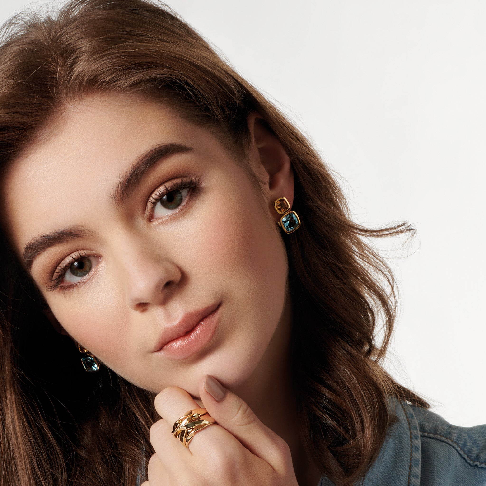 Model wearing handcrafted 18ct yellow gold square shaped earrings featuring citrine and blue topaz gemstones.
