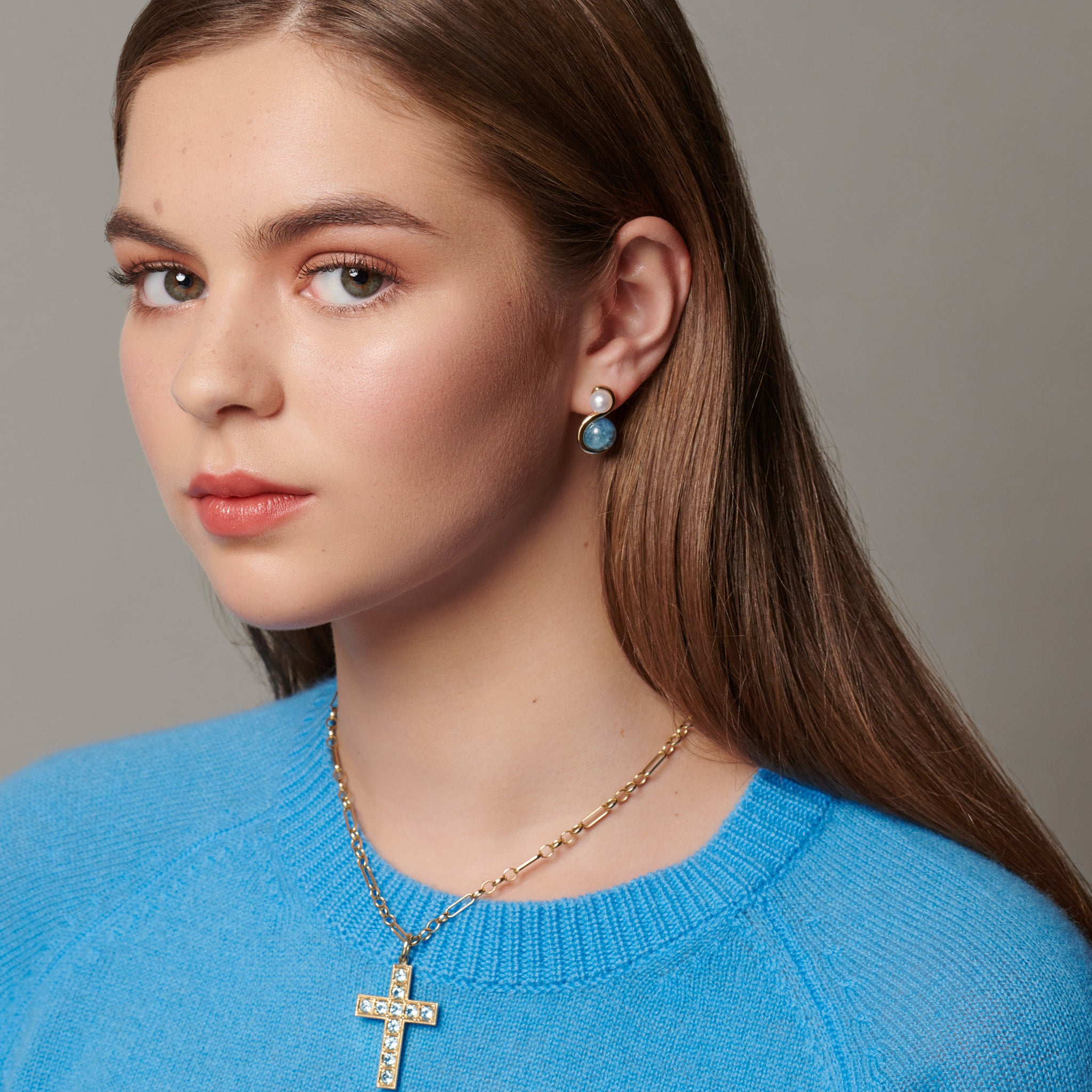 Model wearing handcrafted yellow gold earrings featuring an 's' shape linking the aquamarine and pearl.
