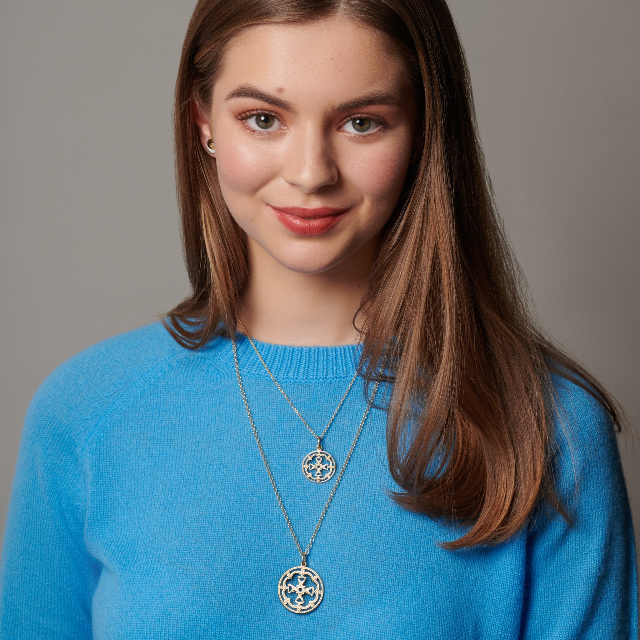 Model wearing two round sterling silver necklace pendants featuring a cross in the middle, hanging from a silver chain.