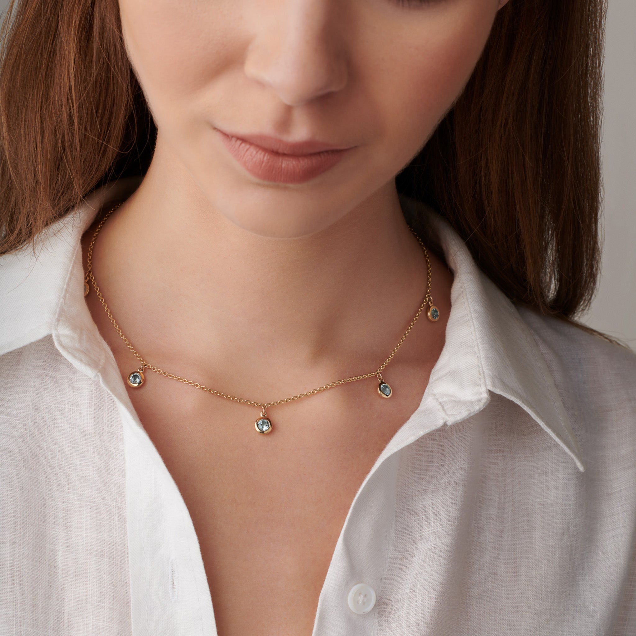 Model wearing a handcrafted necklace in precious metal with five round precious stone drops.