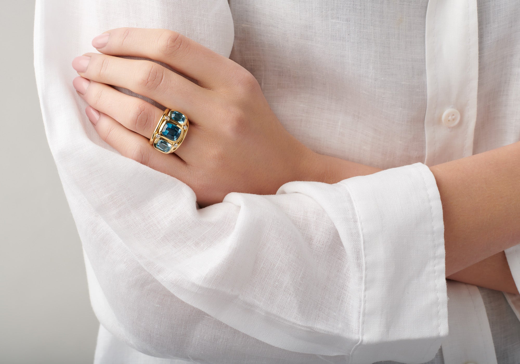 Model wearing a handcrafted 18ct yellow gold ring with blue topaz gemstones.