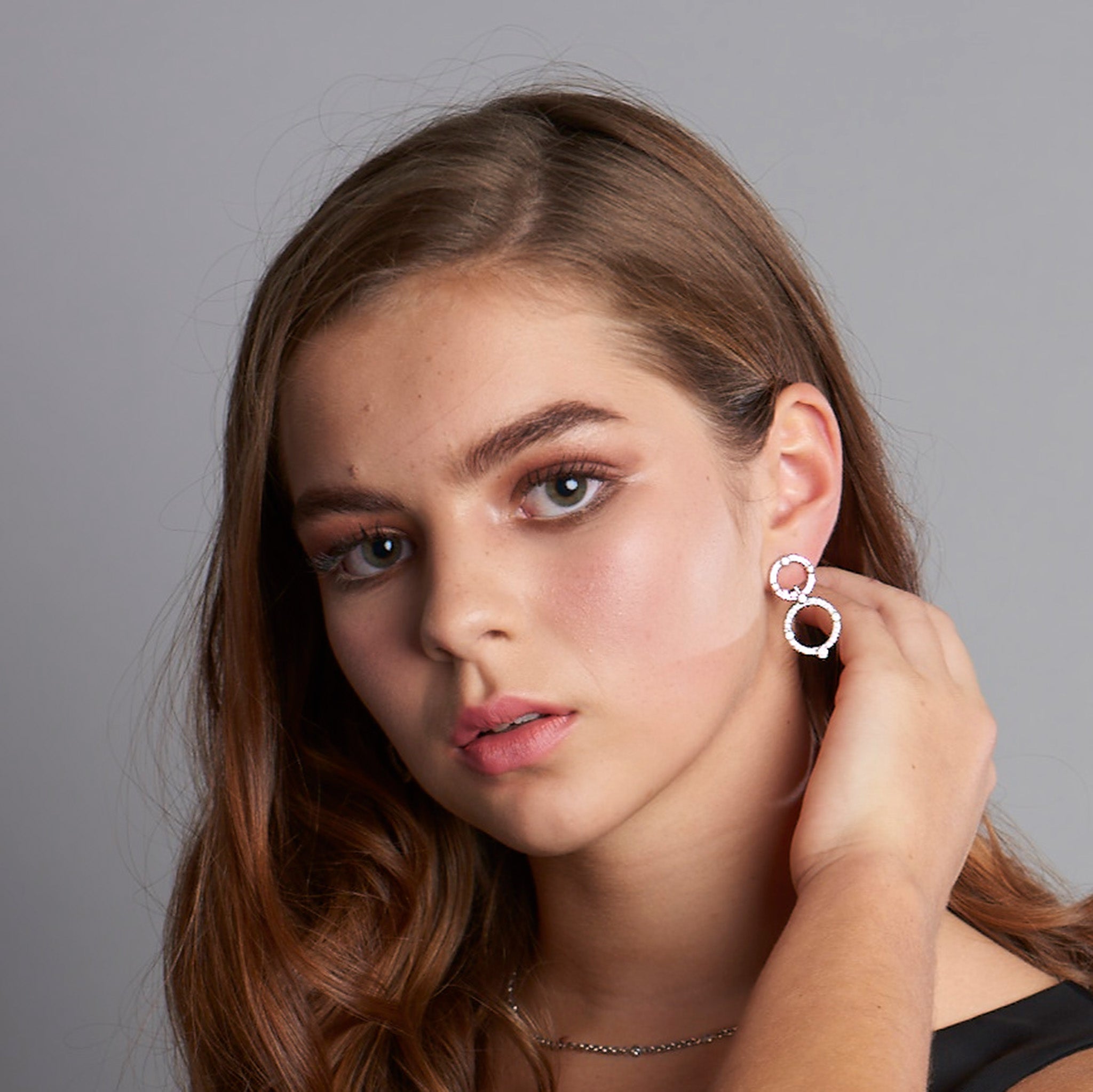 Model wearing handcrafted 18ct white gold earrings featuring two circular shapes with diamonds.
