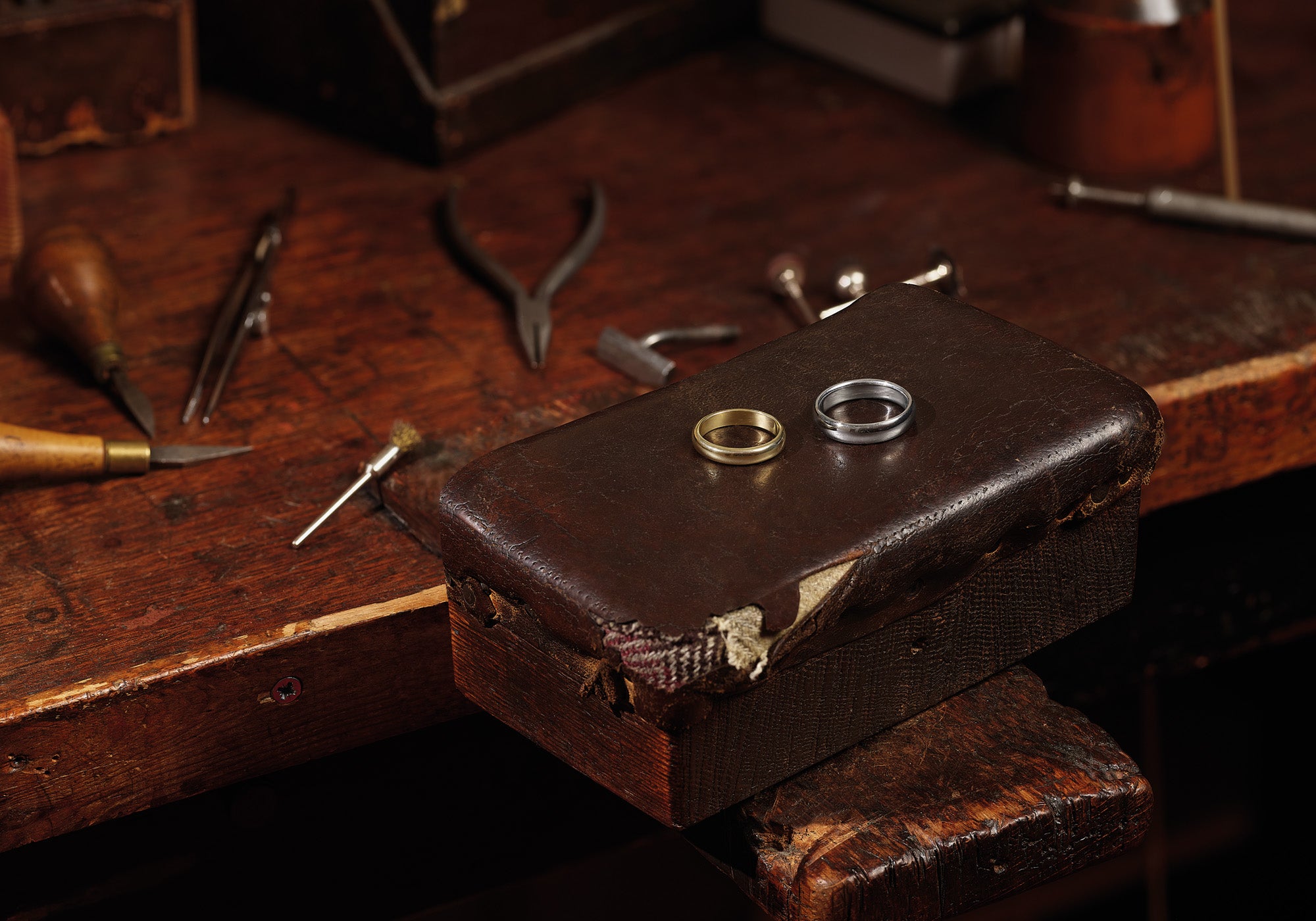 Handcrafted white and yellow gold wedding bands on a workshop bench.