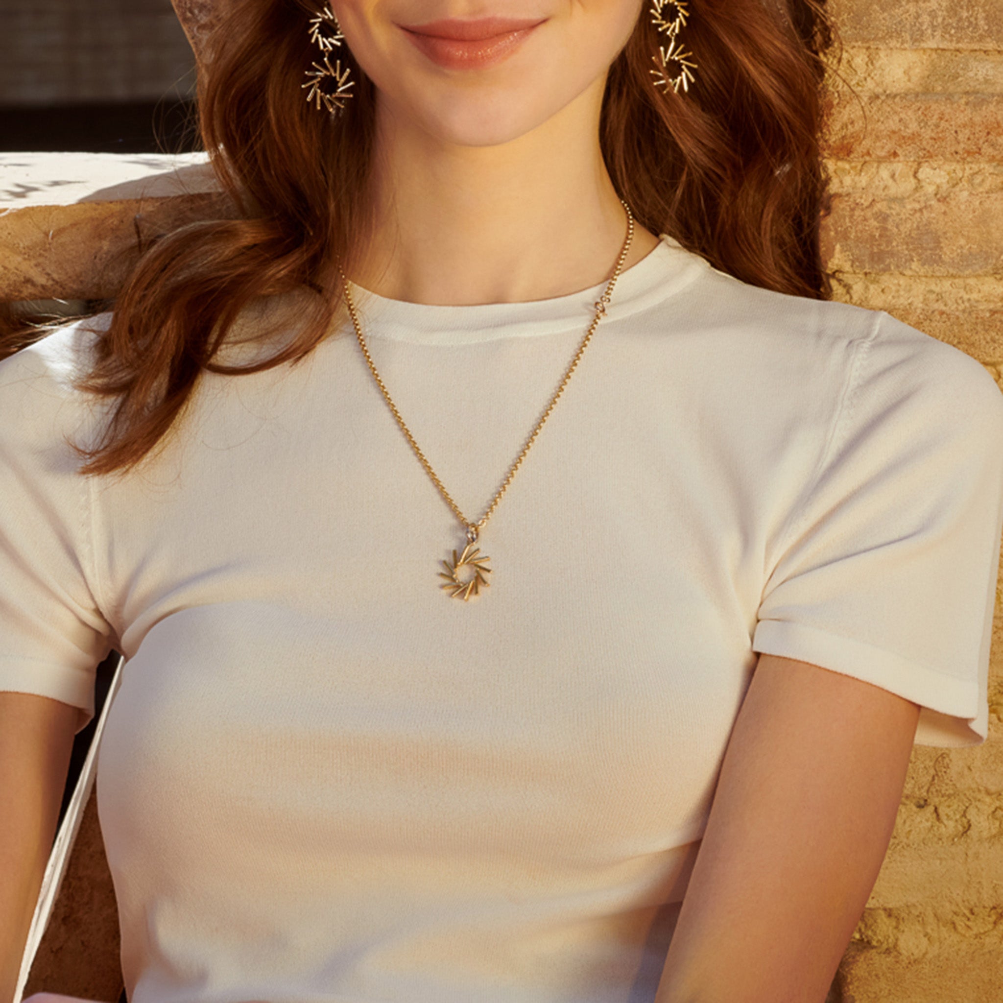 Model wearing a handcrafted yellow gold necklace pendant featuring a circular shape of diagonal lines.
